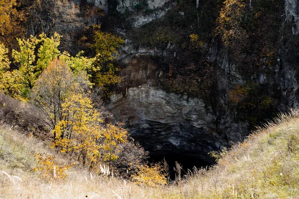 Egy sziklás szikla az erdő közepén, egy veszélyes barlang bejárata. Barlangok, sziklák és vadon élő állatok felfedezése — Stock Fotó