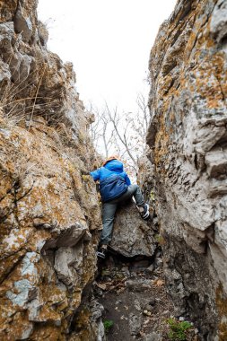 Küçük bir çocuk bir kayaya tırmanarak dağları fetheder. Çocukların aktif turizmi. Dağlarda tek başına yürüyüş. Çocuk sonbaharda doğada sıcacık giyinir. Yüksek kalite fotoğraf