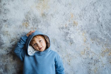 Mavi takım elbiseli bir çocuk elini başının üstünde tutuyor. Hafif bir arkaplanda çekilmiş..