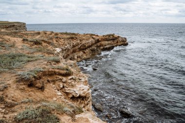 Bir deniz pelerininin yakın çekimi, kayalara vuran dalgalar, kalın deniz köpüğü. Ebb ve gelgitler. Bulutlu bir günde deniz kıyısında yürümek.
