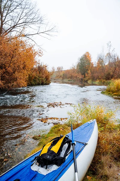 Turistico kayak blu per il rafting sui fiumi di montagna si trova sulla riva del fiume. Uno zaino giallo giace nella barca. Il concetto di rafting sui fiumi taiga. Spedizione autunnale. — Foto Stock