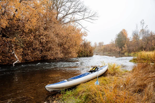 Turista kayak azul para el rafting en los ríos de montaña se encuentra en la orilla del río. Una mochila amarilla yace en el barco. El concepto de rafting en ríos taiga. Expedición de otoño. —  Fotos de Stock