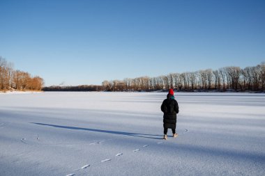 Kışın gölün panoramik manzarası. Genç bir kız donmuş bir gölde yürüyor. Parlak soğuk güneş. Kışın doğa yürüyüşü. Karda ayak izleri. Yüksek kalite fotoğraf