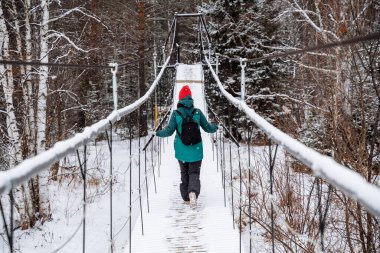 Bir adam donmuş bir nehrin üzerindeki asma köprüde yürüyor. Kışın ormanda daha sık yürüyün, karlı bir ormanda. Tehlikeli bir halat köprüsünde geçiş. Yüksek kalite fotoğraf