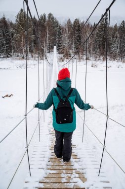 Bir adam donmuş bir nehrin üzerindeki asma köprüde yürüyor. Kışın ormanda daha sık yürüyün, karlı bir ormanda. Çerçeve yukarıda. Yüksek kalite fotoğraf