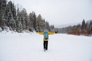 Parlak sırt çantalı neşeli bir gezgin orman boyunca yürüyor. Karlı orman ve kayalar. Kışın dağa tırmanmak. Vahşi doğada hayatta kalmak. Yüksek kalite fotoğraf