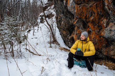 Bir gezgin kayanın yanındaki termostan çay içer. Çalı işi. Kışın kaya tırmanışı. Dağlara doğru vahşi doğaya bir yolculuk. Dağlarda dinleniyor. Yüksek kalite fotoğraf