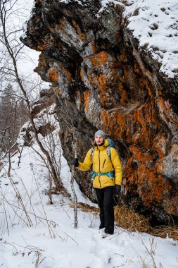 Gezgin uçurumun kenarında duruyor. Karlı orman ve kayalar. Sopa, destek için baston. Kışın dağa tırmanmak. Vahşi doğada hayatta kalmak. Yüksek kalite fotoğraf