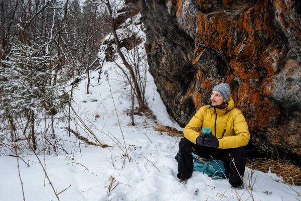 Bir gezgin kayanın yanındaki termostan çay içer. Çalı işi. Kışın kaya tırmanışı. Dağlara doğru vahşi doğaya bir yolculuk. Dağlarda dinleniyor. Yüksek kalite fotoğraf