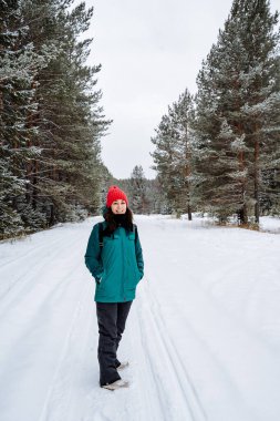 Mutlu ve gülümseyen kız kış ormanında yürüyor. Kış geliyor. Karla kaplı ormanlar. Kış mevsiminde yürüyüş. Parlak kış ekipmanları. Yüksek kalite fotoğraf