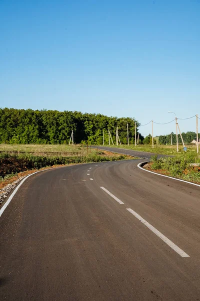 Droga motorowa. Pusta asfaltowa droga z zakrętem między łąkami kwiatowymi na wsi. Wycieczka w słoneczny dzień w lecie — Zdjęcie stockowe