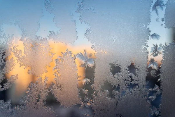 Frostiges Muster auf dem Fenster, Sonnenuntergangsstrahlen durchdringen das Glas. Ein ungewöhnliches Naturphänomen im Winter. Entnahme von gefrorenem Wasser — Stockfoto