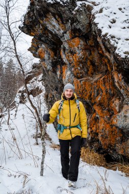 Gezgin uçurumun kenarında duruyor. Karlı orman ve kayalar. Sopa, destek için baston. Kışın dağa tırmanmak. Vahşi doğada hayatta kalmak. Yüksek kalite fotoğraf