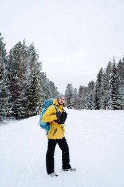 Parlak sırt çantalı neşeli bir gezgin orman boyunca yürüyor. Karlı orman ve kayalar. Kışın dağa tırmanmak. Vahşi doğada hayatta kalmak. Yüksek kalite fotoğraf