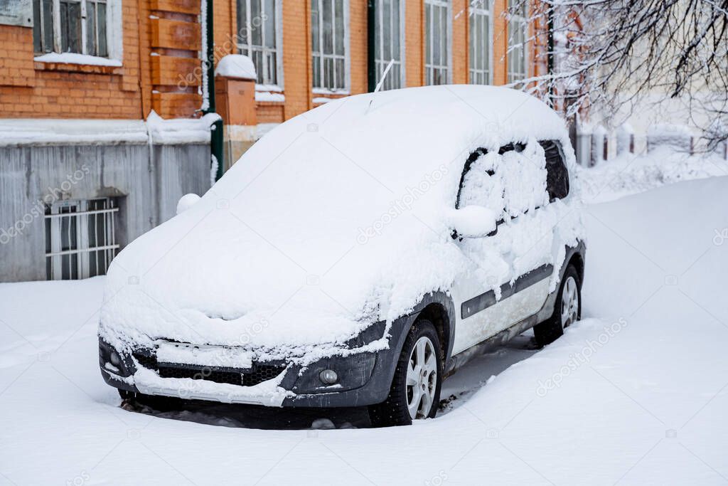 The car is covered with snow. Snowfall in the city. Equipment under the snowdrift. The car got stuck in the snow in the winter. Uncleaned streets of the metropolis. High quality photo