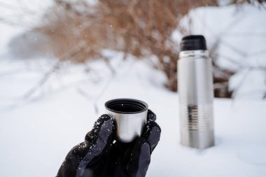 A cup of hot tea from a thermos. Drink coffee in nature. Metal thermal mug made of steel. A bottle that retains heat. Picnic utensils, camping kit. High quality photo