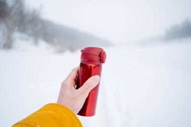A person holds a thermos with a hot drink in his hand. The concept of winter recreation in nature. High quality photo