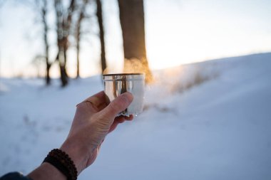 A cup of hot tea from a thermos. Drink coffee in nature. Metal thermal mug made of steel. A bottle that retains heat. Picnic utensils, camping kit. High quality photo