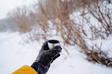 A hand holds a mug of hot tea. Drink tea in nature. A glass of hot coffee in the forest. High quality photo