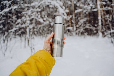 Hold a gray thermos with tea in your hand. Metal thermos of silver color. Made of steel. High quality photo