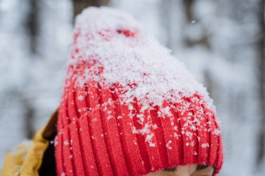 Kar taneleri kırmızı şapkanın üzerinde yatar. Beyaz kar kıyafetlerin üstüne düşer. Sıcak kış şapkası. Örgü başlık. Yüksek kalite fotoğraf