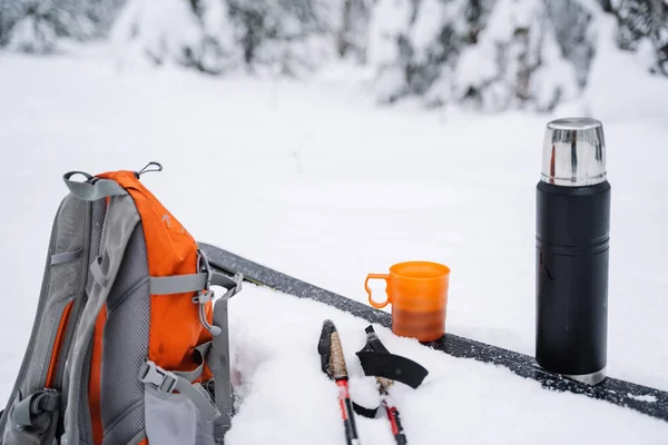 雪の中のスキー場には紅茶のマグカップ付きの黒い魔法瓶 雪の中には鮮やかなオレンジ色のハイキングバックパックが横たわっている 冬のスキー 高品質の写真 — ストック写真