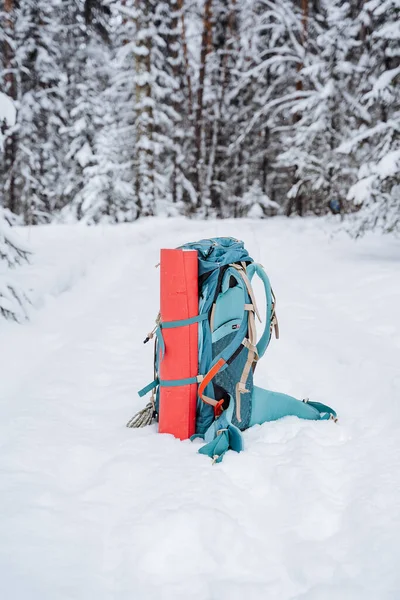 Una brillante mochila de senderismo yace en la nieve. Una cuerda de escalada está atada a una mochila. En el bolsillo lateral del termo. Senderismo en invierno. Rocas y bosques —  Fotos de Stock