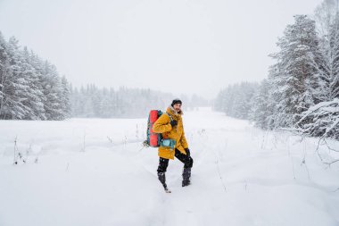 Sırtında yürüyüş çantasıyla gülümseyen ve mutlu bir gezgin. Karlı orman ve kayalar. Kışın dağa tırmanmak. Vahşi doğada hayatta kalmak. Yüksek kalite fotoğraf