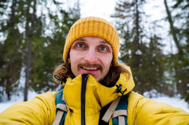 Karla kaplı bir ormanda mutlu bir adamın portresi. Kocaman bir gülümseme, ağzından buhar fışkırıyor, neşeli gözler. Isınmak için parlak kışlık giysiler. Yüksek kalite fotoğraf