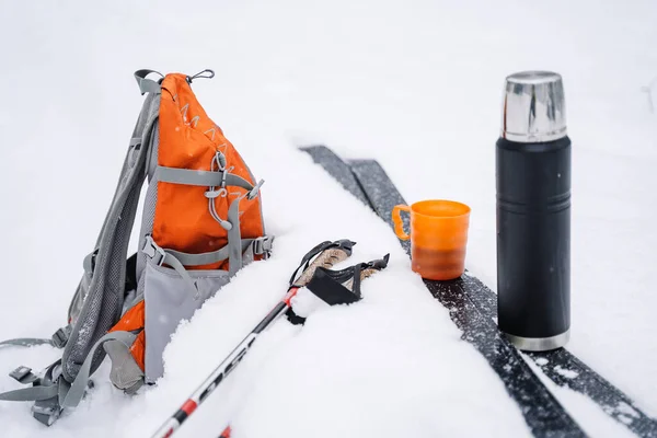 雪地里 一个装有茶杯的黑色热水瓶站在雪地上 雪地里躺着一个明亮的橙色远足背包 在冬天滑雪 高质量的照片 — 图库照片