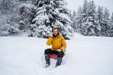 Ormanda telefonla konuşan sevimli bir gezgin. Karlı orman ve kayalar. Kışın dağa tırmanmak. Vahşi doğada hayatta kalmak. Yüksek kalite fotoğraf