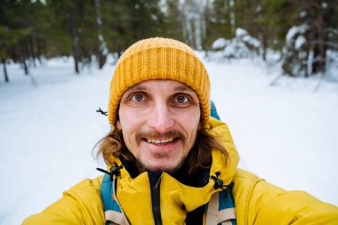 Parlak elbiseli çekici bir adamın portresi. Orman kasesinde selfie çeken bir adam. Gezginin yüzünde kocaman bir gülümseme. Kışın ormanda yürüyorum. Yüksek kalite fotoğraf