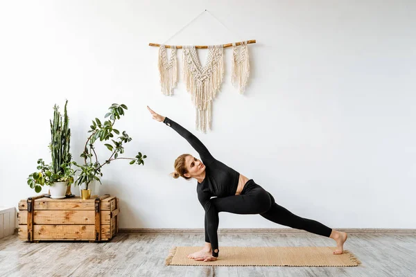 Kız siyah spor bir takım elbiseyle yoga yapıyor. Savaşçının duruşunun çeşitliliği. VIRABHADRASANA. Yoganın ilk elementleri ustalaşıyor. İyi esneme ve nefes kontrolü. Yüksek kalite fotoğraf