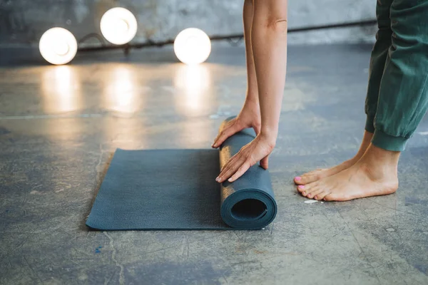 Bir kız yoga için elinde minderle yerde duruyor. Arka ışık öne doğru parlıyor. Yalnız kalmak, evde meditasyon yapmak, spor için bir yer hazırlamak. Yüksek kalite fotoğraf