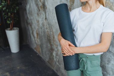 Bir kız elinde bir yoga minderi tutuyor belindeki mavi kauçuk paspasın yakın plan fotoğrafını bir kadının vücudunun arka planına yani fitness derslerine karşı tutuyor. Yüksek kalite fotoğraf