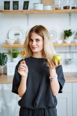 Mutfakta bir kız elinde bir elmayla kameraya bakıyor. Güzel genç bir kadın ev mutfağında duruyor. Yemeği elinde tut. Hileli bir bakış. Yüksek kalite fotoğraf