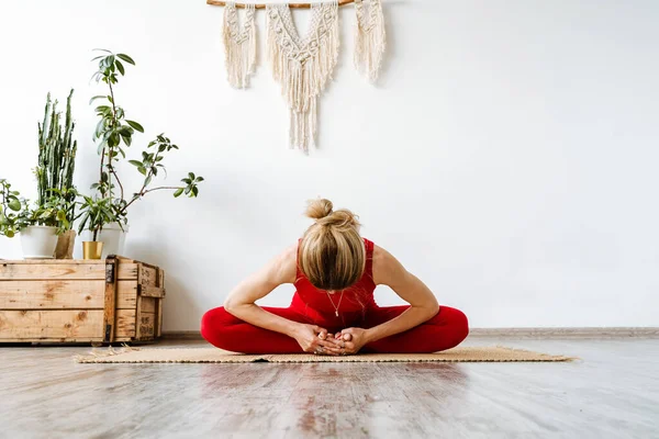 Kırmızı eşofmanlı genç bir kız evde yoga yapıyor. Odasında asana dansı yapan bir kadın yerde oturup kaslarını esnetiyor. Yüksek kalite fotoğraf
