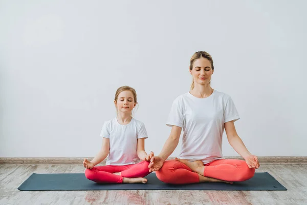Aile çemberinde çift yoga. Anne ve kızı kelebek pozunda oturur, gözleri kapalı meditasyon yapar. Baddha Konasana. Huzur ve huzur..