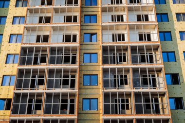 Bir konut inşaatı. Binanın ön cephesi pencereli, alüminyum çerçeveli bölmeler için. Evi mineral yünüyle yalıtın. İnşaat alanının dış işleri.