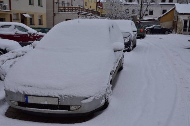 Kasvetli bir kış gününde, şehrin bir caddesindeki otoparkta karla kaplı arabalar..
