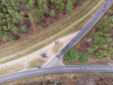 Sonbaharda sık bir ormanda asfalt ve orman yollarının kesiştiği yer yukarıdan görülüyor. Gün. 