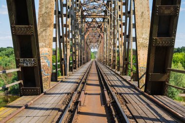 The metal structure of the railway viaduct over the river against the background of a blue sky with clouds. Day. 