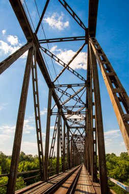 The metal structure of the railway viaduct over the river against the background of a blue sky with clouds. Day. 
