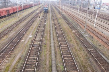 Bulutlu bir sonbahar gününde elektrikli lokomotifler, vagonlar, demiryolu altyapısı.