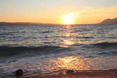 Deniz kıyısındaki plajda yavaşça portakal rengi gün batımı, Hırvatistan 'ın deniz köpüğü ve ıslak kumuna yansıyor. Deniz köpüğü ve turuncu deniz bir yaz akşamında gün batımında.