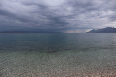 Hırvatistan kıyılarında bir fırtınanın arifesinde kumsal, ufukta kara yağmur bulutları ve sahilde açık deniz suyu.