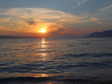 Denizin üzerinde gün batımı, ufuktaki turuncu güneş bir yaz akşamında bulutları ve denizi aydınlatır. Deniz manzaralı gün batımı, bulutlu gökyüzü ve sakin deniz yaz akşamları, Hırvatistan 'da deniz kenarında tatil
