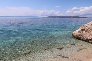 Güneşli bir günde deniz manzarası, kıyıda temiz su ve taşlar. Adriyatik Denizi 'nde tatiller. Hırvatistan 'ın deniz kıyısında resimli deniz kıyısı, ufukta Brac adası, deniz manzarası 