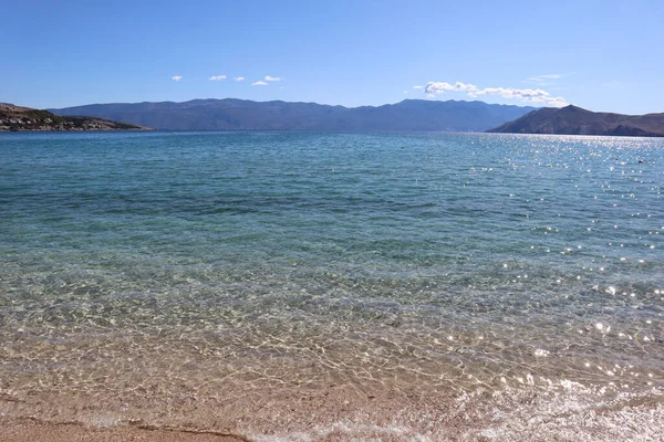 Hırvatistan 'ın Baska kentinde, güneşli bir günde Krk adasında bir plaj. Açık turkuaz suyu ve ufukta bir dağ silsilesi olan bir tatil köyündeki resim gibi bir sahil.