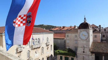 Hırvatistan 'ın mavi gökyüzü ve Hırvatistan' ın eski Trogir kentinin merkez meydanına karşı Hırvat bayrağı. Hırvatistan 'ın eski Trogir, Dalmaçya kentinin tarihi kısmındaki ortaçağ mimarisi, antik binalar, saat kulesi